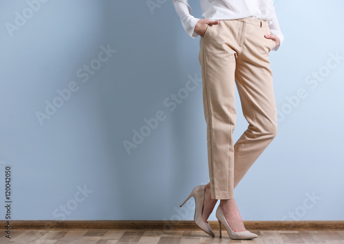 Beautiful young woman in a white shirt and beige pants on blue wall background