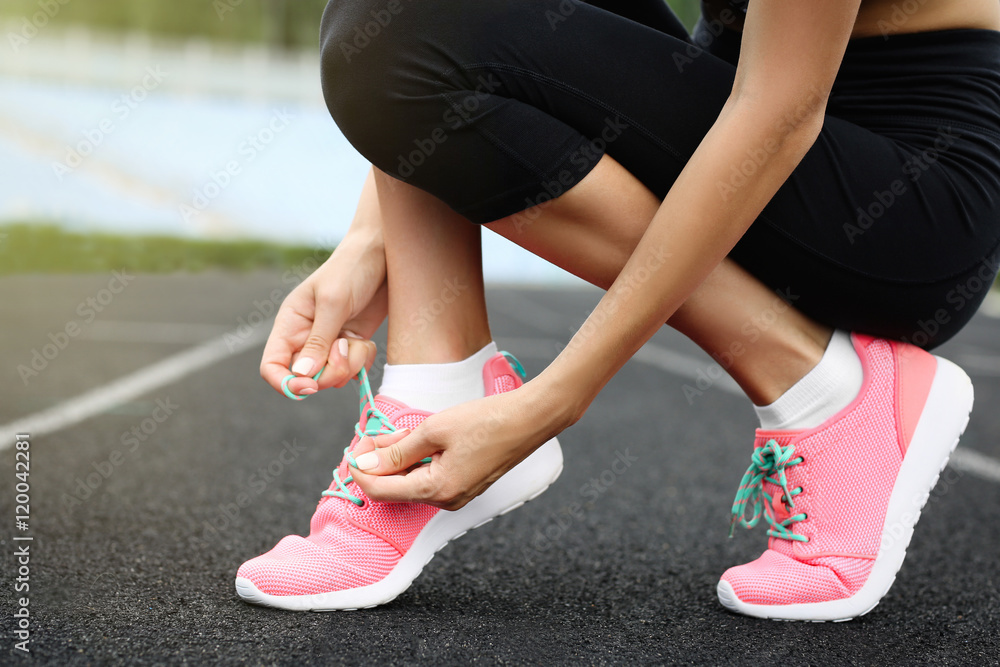 Woman tying lace on her sneakers on a running stadium