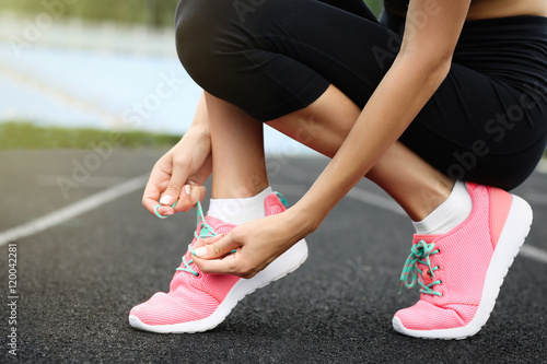 Woman tying lace on her sneakers on a running stadium