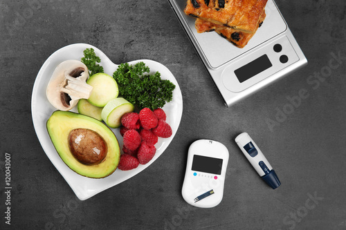 Glucose meter with healthy food and cookies on table