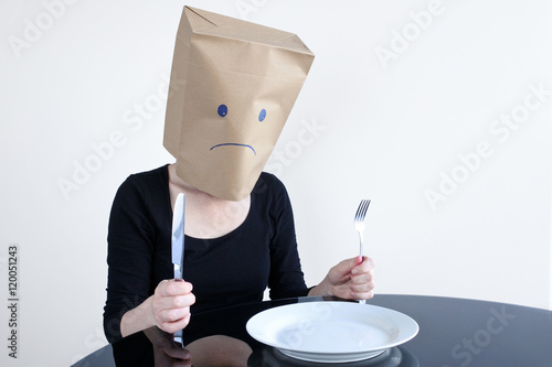 Anonymous sad woman with empty plat sit at the table alone photo