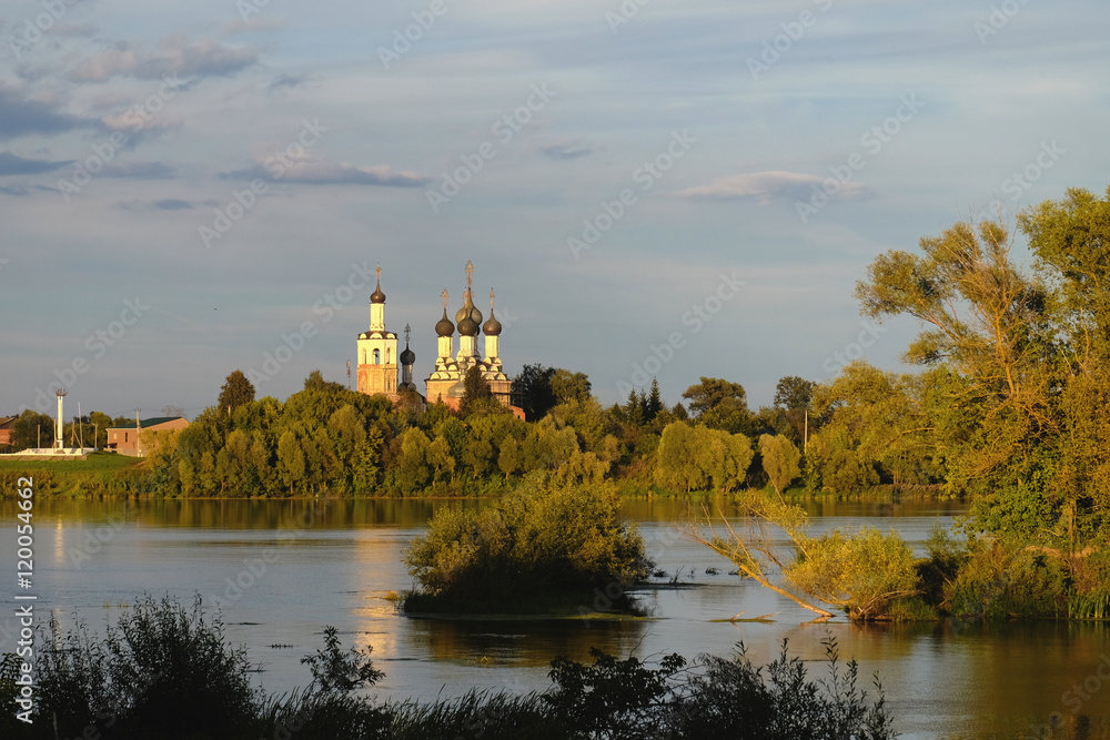 Православный храм на берегу реки в лучах закатного солнца