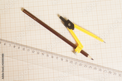Yellow Drawing compass with black pencil and ruler on graph pape