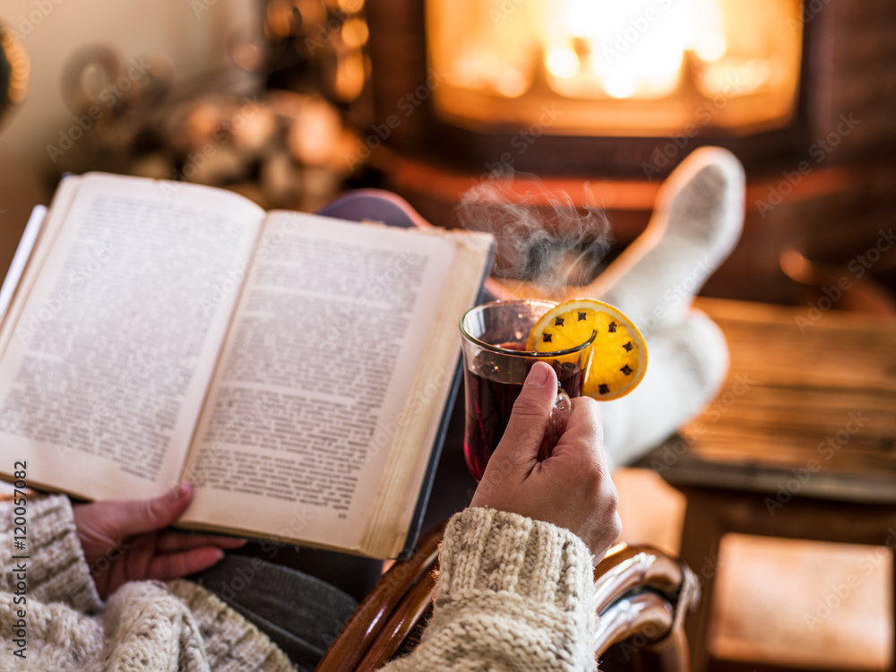 Fototapeta premium Hot mulled wine and book in woman hands. Relaxing in front of bu