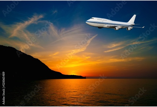 passenger airplane in the clouds at sunset or dawn. Tourist Card. plane on a background of sea and mountains. travel by air transport. flying to the top of the airliner. nobody