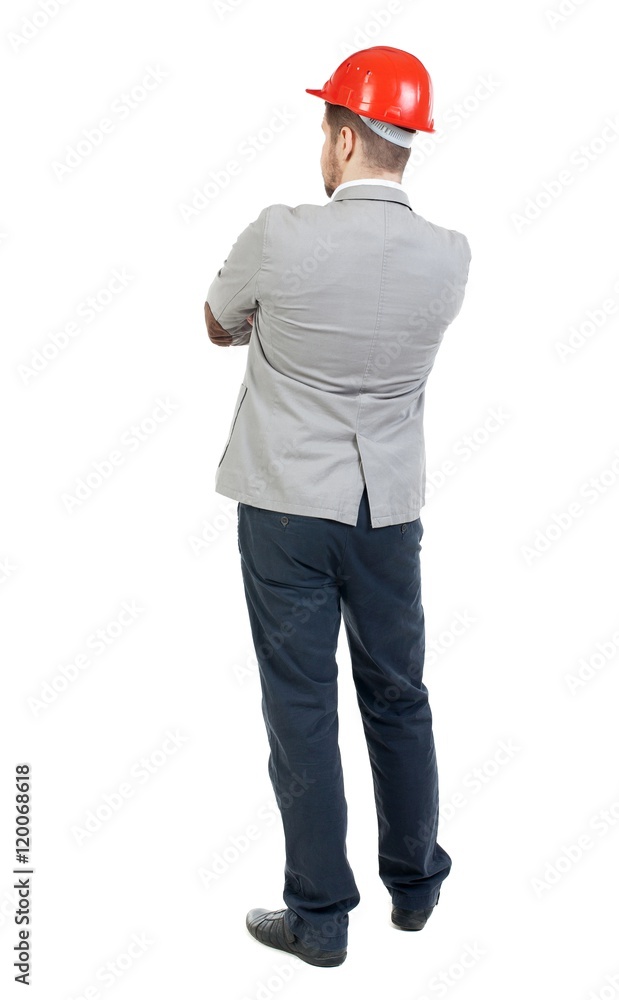 Backview of an engineer in construction helmet stands. bearded man in a gray suit and an orange helmet stands with his arms folded. Backview of an engineer in construction helmet stands. bearded man in a gray suit and an orange helmet stands with his arms folded.