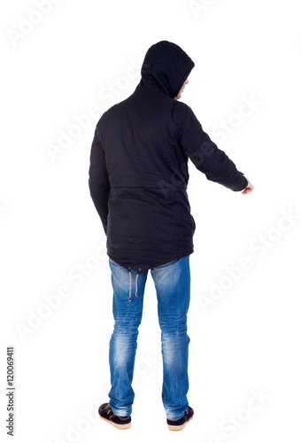 Back view of pointing young men in parka. Young guy gesture. Rear view people collection. The guy while wearing a hood on his head is pointing down.