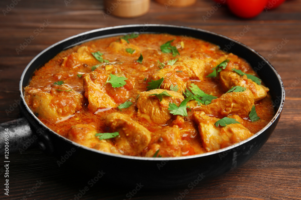 Tasty chicken curry in pan on wooden background