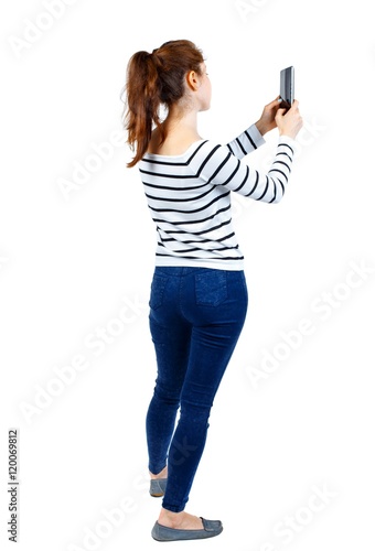 back view of standing young beautiful woman using a mobile phone. girl watching. Girl in a striped sweater photographing something on the side of the tablet.