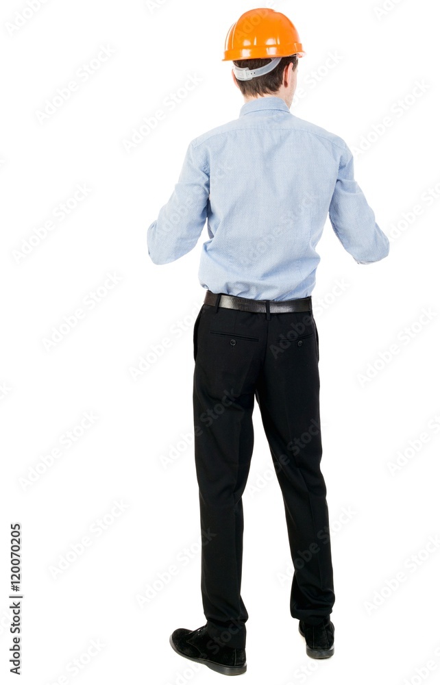 Backview of an engineer in construction helmet stands. Curly businessman in a light jacket and a helmet peering forward. Backview of an engineer in construction helmet stands. Curly businessman in a light jacket and a helmet peering forward.