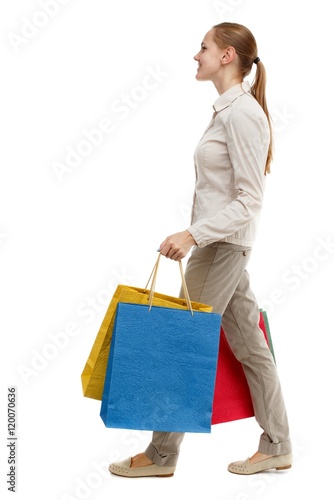 side view of going woman with shopping bags . Rear view people collection. Isolated over white background. Skinny girl in white jeans walks past with purchases.