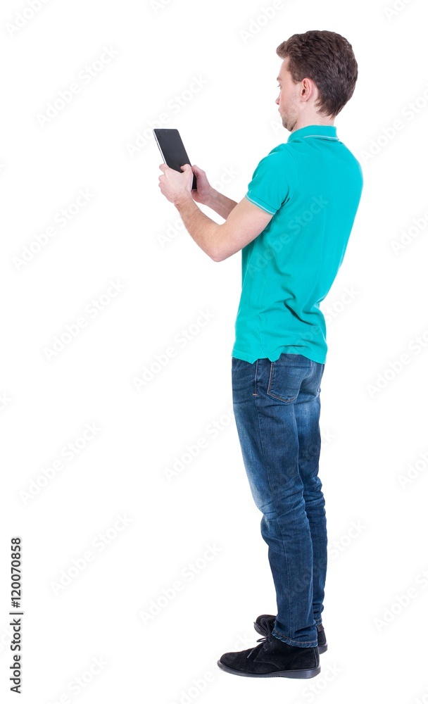 back view of standing business man photographing a phone or tablet. Curly man in turquoise blouse standing side by playing the game on the tablet. back view of standing business man photographing a phone or tablet. Curly man in turquoise blouse standing side by playing the game on the tablet.