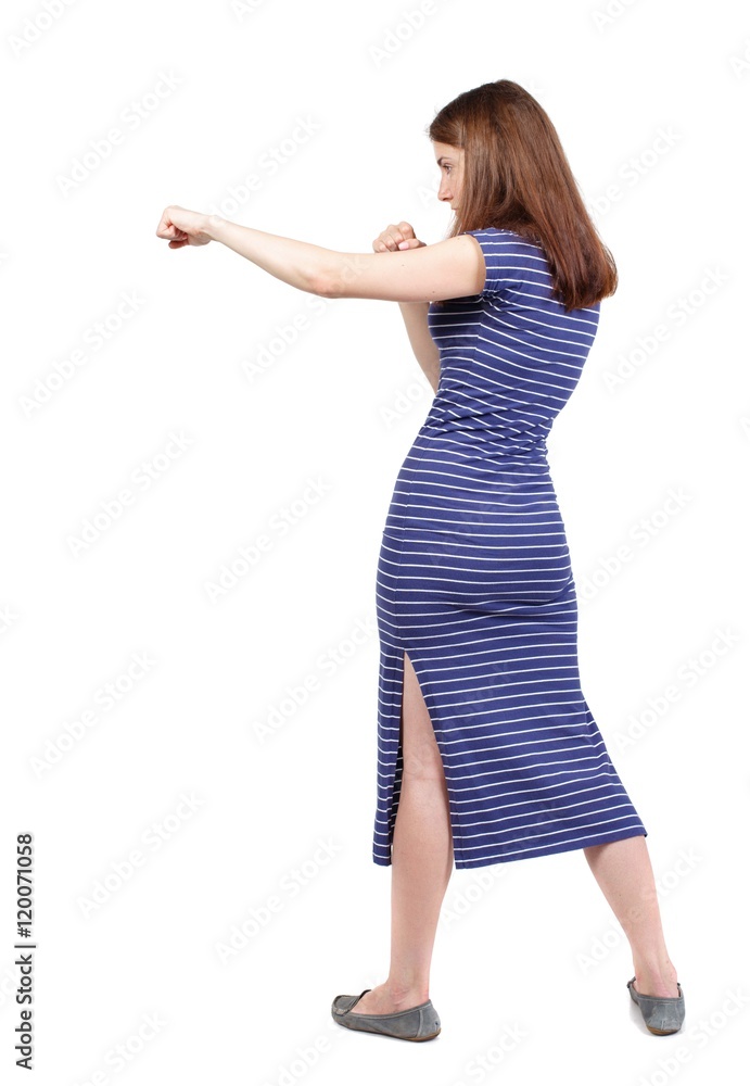 skinny woman funny fights waving his arms and legs. brunette in a blue striped dress stands sideways and hit his foot. skinny woman funny fights waving his arms and legs. brunette in a blue striped dress stands sideways and hit his foot.