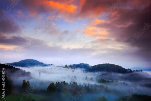 Foggy morning with beautiful orange clouds. Cold misty foggy morning in a fall valley of Bohemian Switzerland park. Hills with fog, landscape of Czech Republic, National Park Ceske Svycarsko