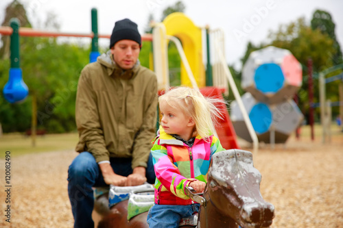  little girl with her father on outdoor playground equipment