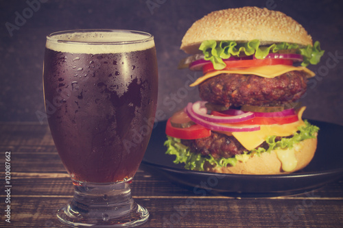 Glass of Dark Beer and  Delicious Burger With Beef, Tomato, Cheese, Lettuce and Onion photo