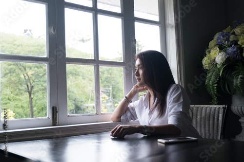 Thai attractive girl is sitting and looking for something outside the window.