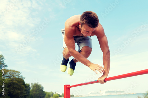 young man exercising on horizontal bar outdoors © Syda Productions