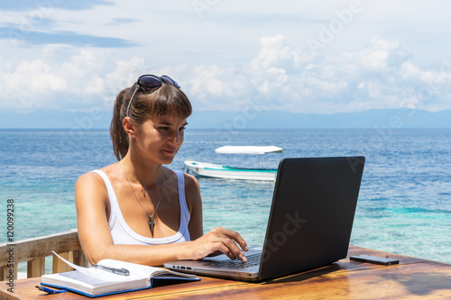 yung pretty woman freelancer writer working with laptop notepad and phone infront of blue tropical sea