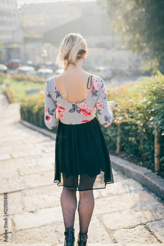 From behind view of young beautiful blonde woman walking outdoor in the street of the city
