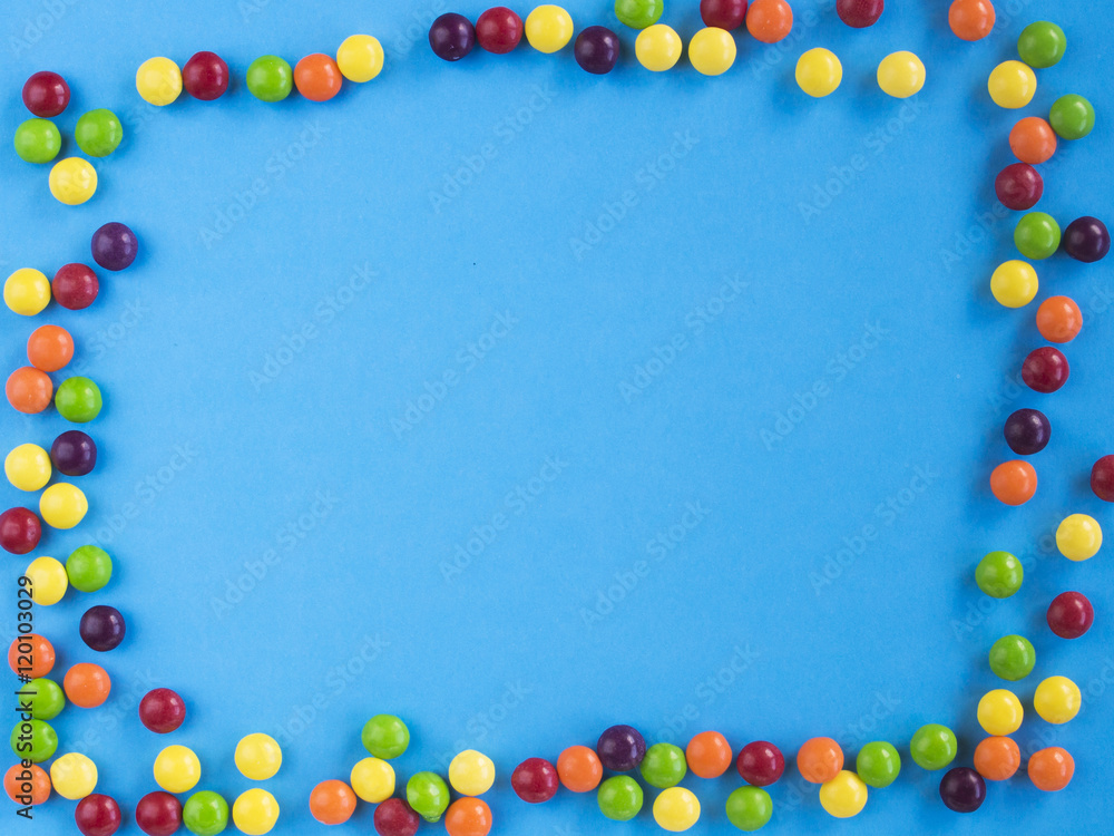 Frame of multicolored small candie on blue background. Copy space for text. Flat lay. Top view Frame of multicolored small candie on blue background. Copy space for text. Flat lay. Top view