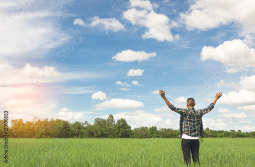 Enjoyment - free happy young man enjoying sunrise. The young man in plaid shirt with arms outspread and face raised in sky enjoying peace, serenity in green meadow