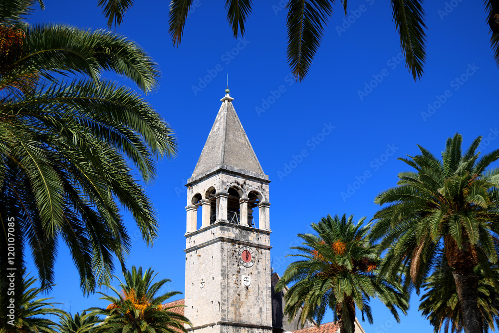 The bell tower of the Saint Dominican convent and church in Trogir, Croatia, surrounded with palm trees. Trogir is popular travel location and UNESCO World Heritage Site.