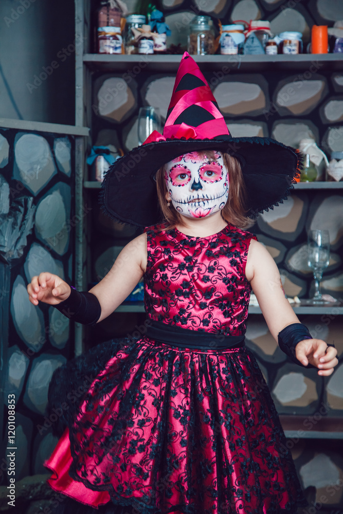 Girl in witch costume and makeup on her face standing in halloween decorations