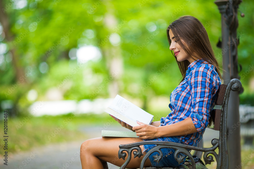 smiling college girl is holding book are sitting in the park. smiling college girl is holding book are sitting in the park.