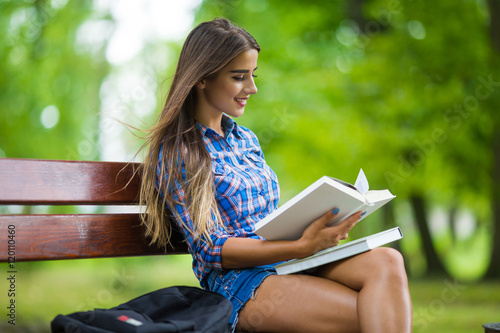 smiling college girl is holding book are sitting in the park.