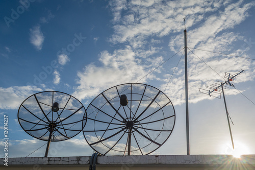 Two black satellite dishes on the rooftop with beautiful blue sk