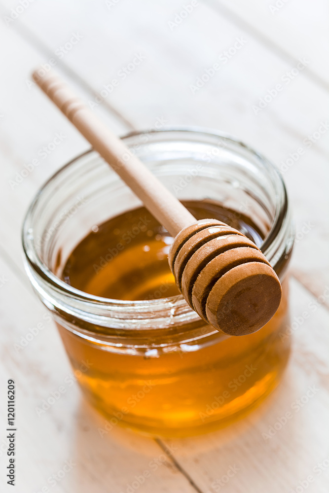 Honey dipper with honey in a jar on white wooden table
Honey dipper with honey in a jar on white wooden table