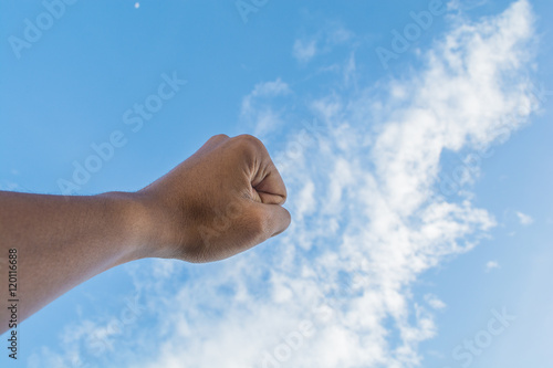 Asian man's fist raised into bright blue sky shows concepts of s