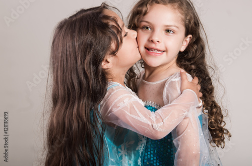 Adorable big and little sister wearing matcing blue dresses posing together happily, studio background photo