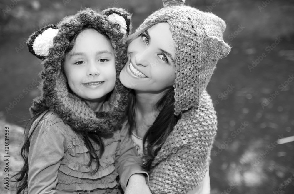 Mother with daughter both wearing hoodies and warm clothing sitting outdoors embracing happily, green nature background, black white edition Mother with daughter both wearing hoodies and warm clothing sitting outdoors embracing happily, green nature background, black white edition
