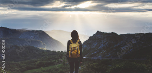 Hipster young girl with backpack enjoying sunset on peak mountain. Tourist traveler on background valley landscape view mockup. Hiker looking sunlight flare in trip in Spain basque country Europa