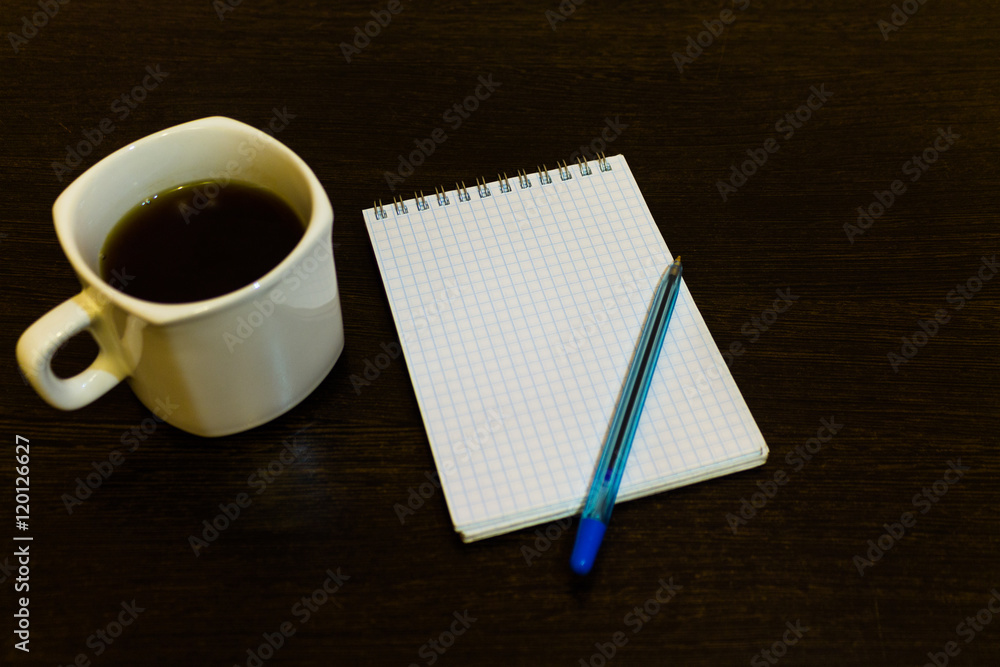 White notepad with a pen on a brown table with a cup of coffee White notepad with a pen on a brown table with a cup of coffee