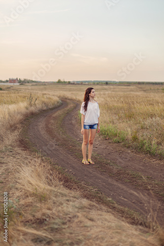 Young girl with brown hair stays at the road in autumn field