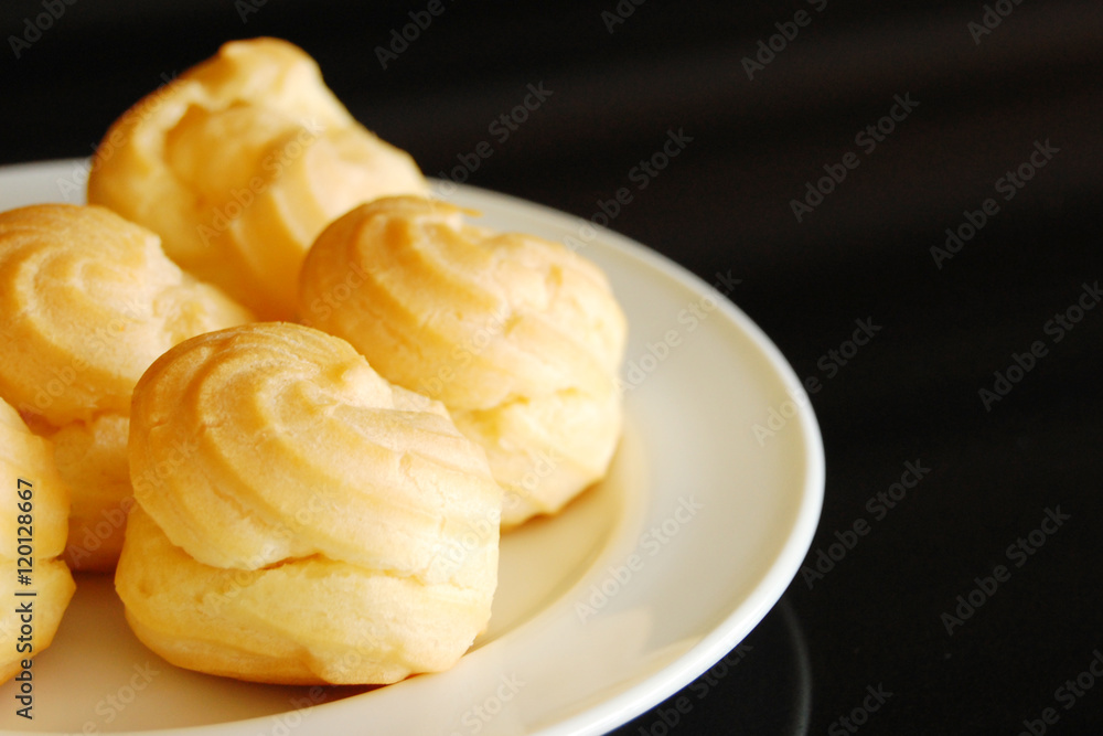 Eclairs or profiterole with chocolate and whipped cream preparing on baking sheet. Spreading chocolate on top of eclair with spoon. Traditional French dessert. Empty space for design text template. Eclairs or profiterole with chocolate and whipped cream preparing on baking sheet. Spreading chocolate on top of eclair with spoon. Traditional French dessert. Empty space for design text template.
