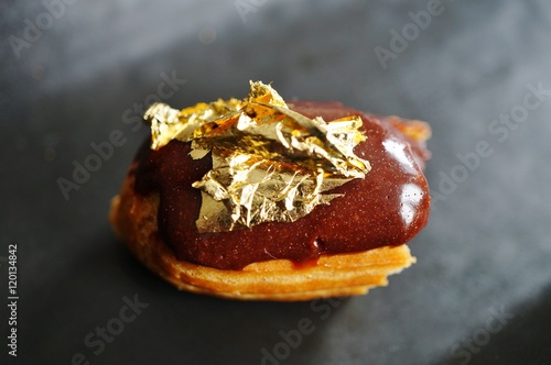 Принти на полотні Bite of a chocolate eclair pastry with an edible gold leaf on top