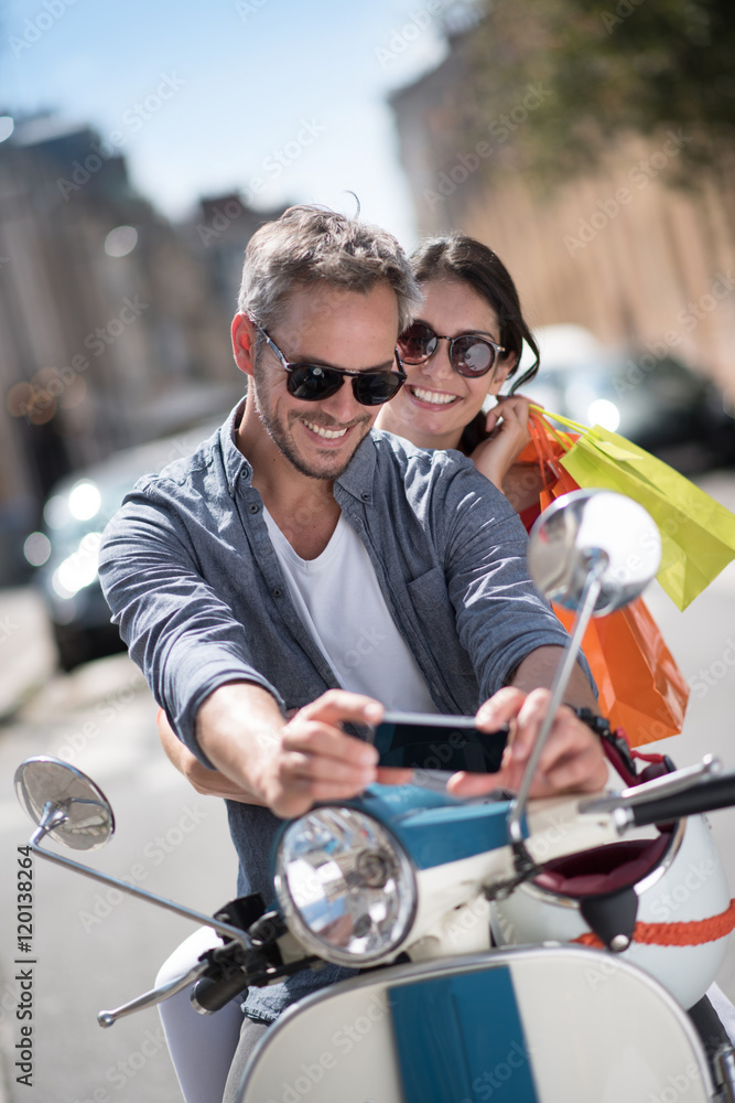 A couple on a scooter in the city, the man takes a selfie