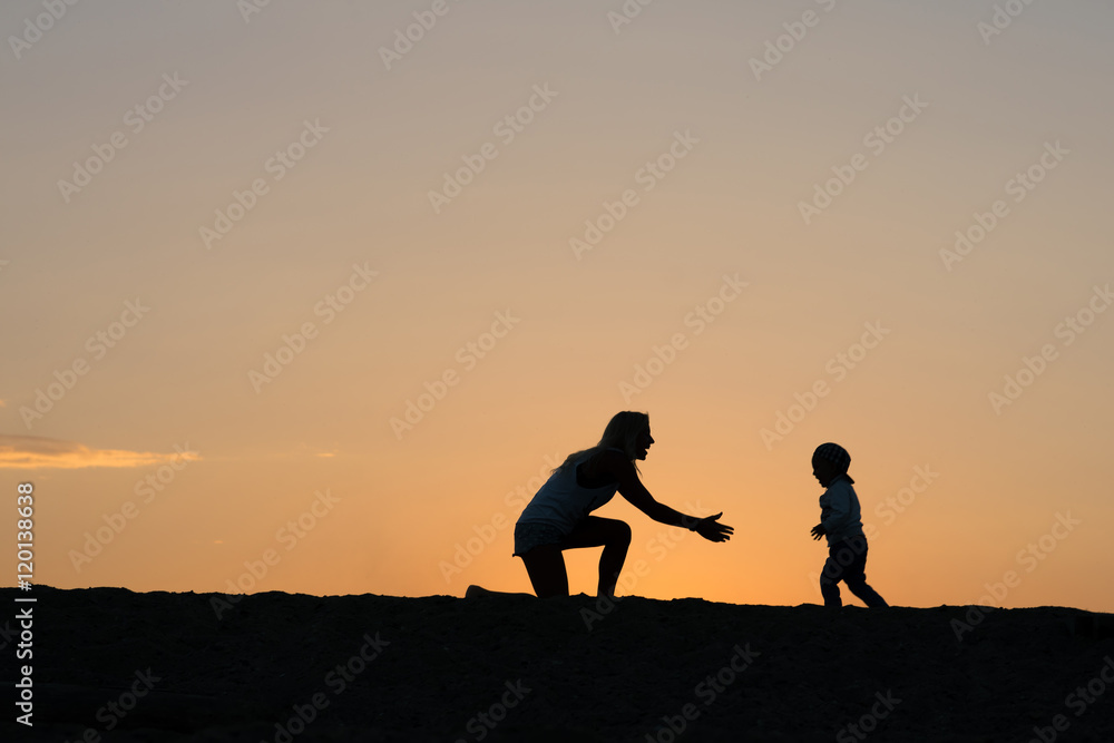 Young mother and her son playing on the beach at the sunset time.