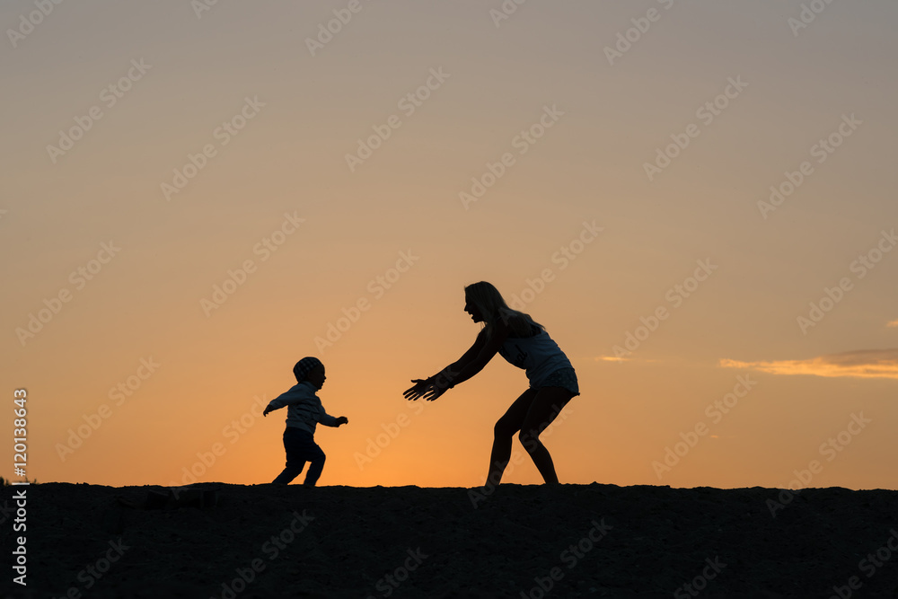 Mother and son playing on the beach at the sunset time.