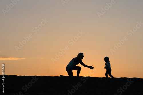 Young mother and her son playing on the beach at the sunset time.