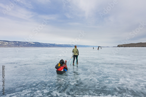 Girl with a sledge and trekking pole is on the ice of Lake Baika
