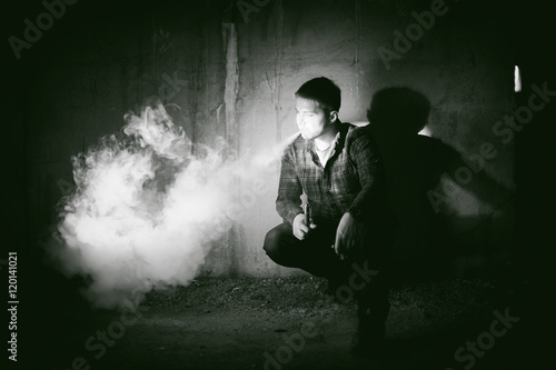 man in a plaid shirt and jeans, smokes an electronic cigarette, blowing smoke and steam from the vaporization a mechanical device. fashionable hobby, alternative to smoking cigarettes, glycerin clouds