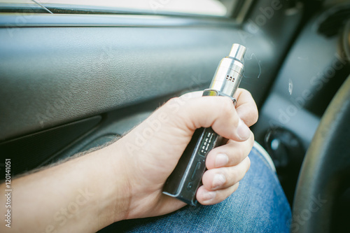 man holding electronic cigarette in her hand sitting in the car. chnrnaya and silver emits vapor. new technologies, alternative smoking without nicotine, harmful to health.