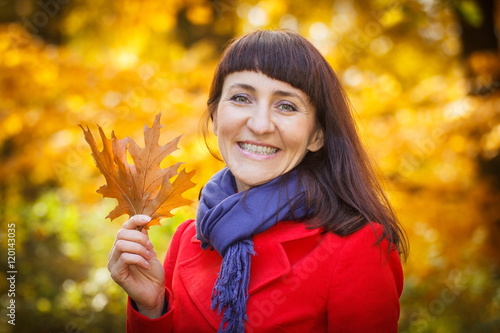 Smiling woman in autumn park with orange leaves in hands