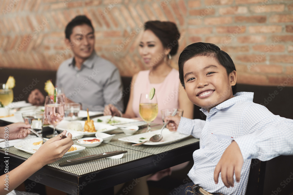 Cheerful little boy sitting at table during family dinner Cheerful little boy sitting at table during family dinner