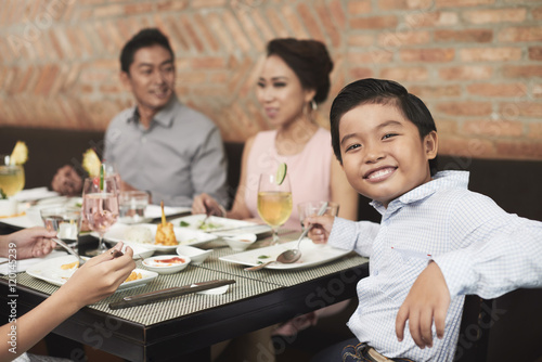 Cheerful little boy sitting at table during family dinner